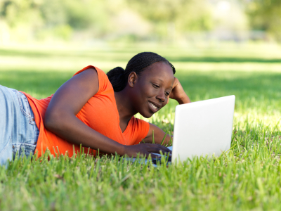 women relaxing on lawn while using laptop