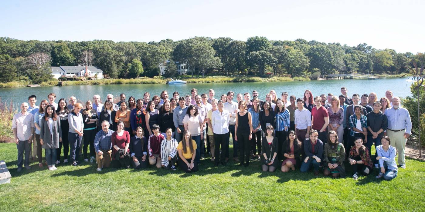 Large group photo outdoors in front of a river on a sunny day